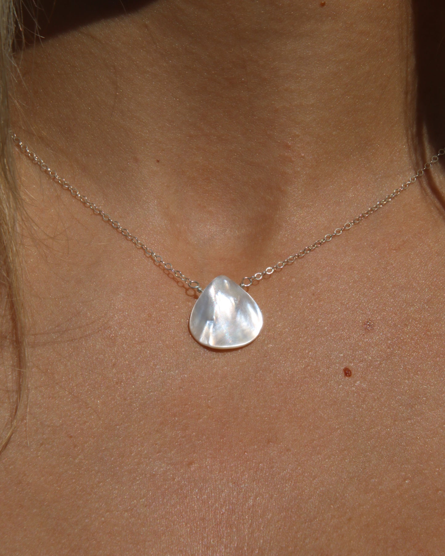 Necklace with a triangle shaped pearl on a person's neck
