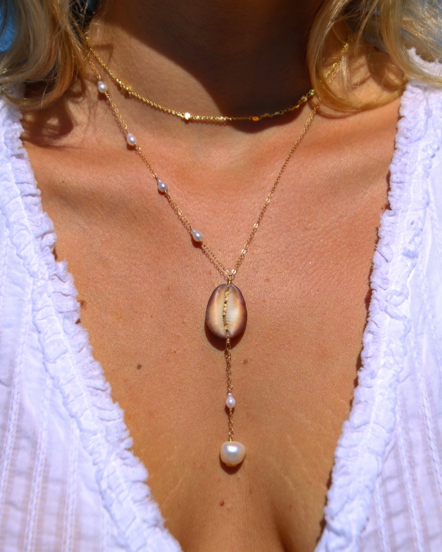 Close-up of a necklace with a pendant on a person wearing a white top.