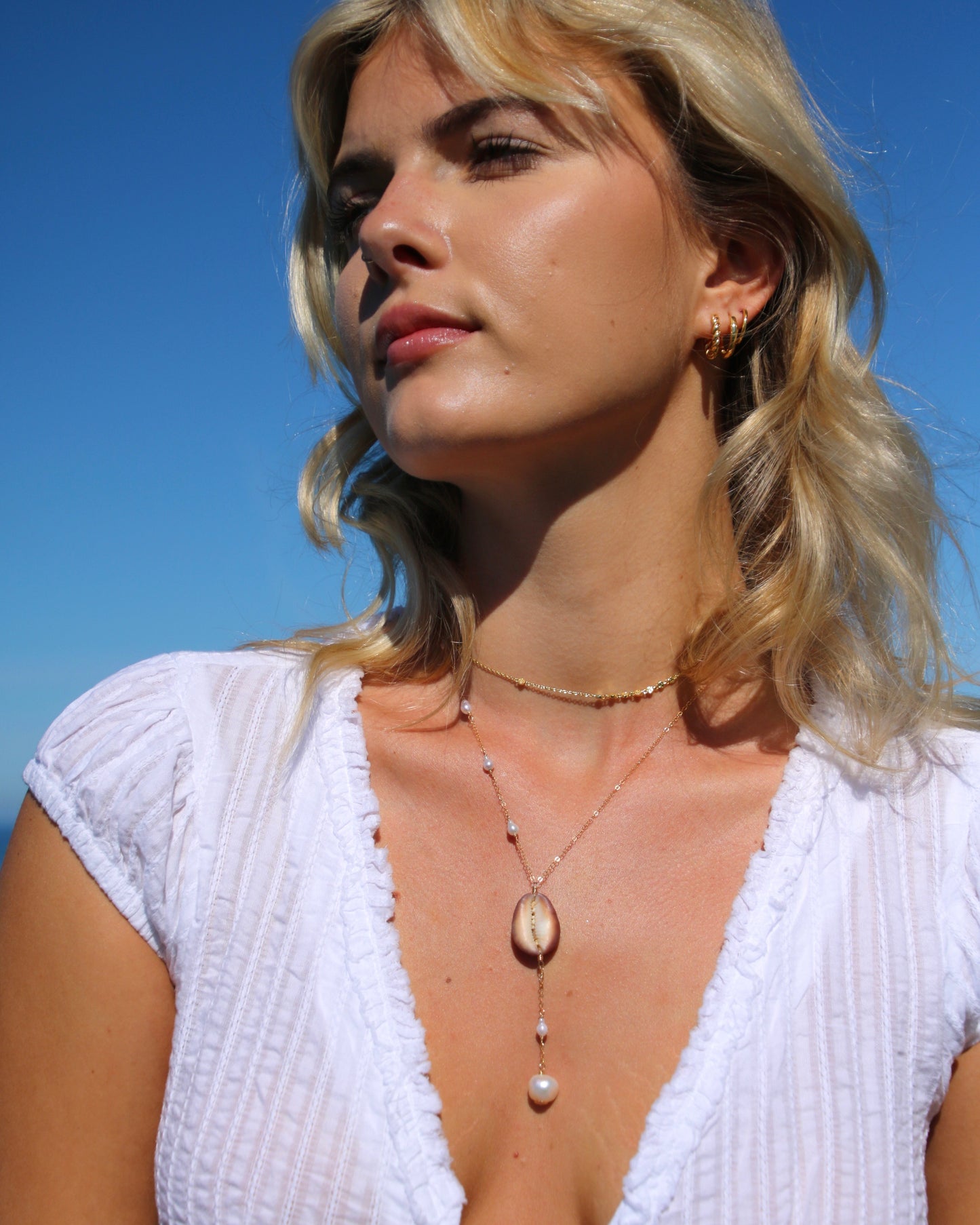 Woman wearing a white dress with a necklace against a clear blue sky