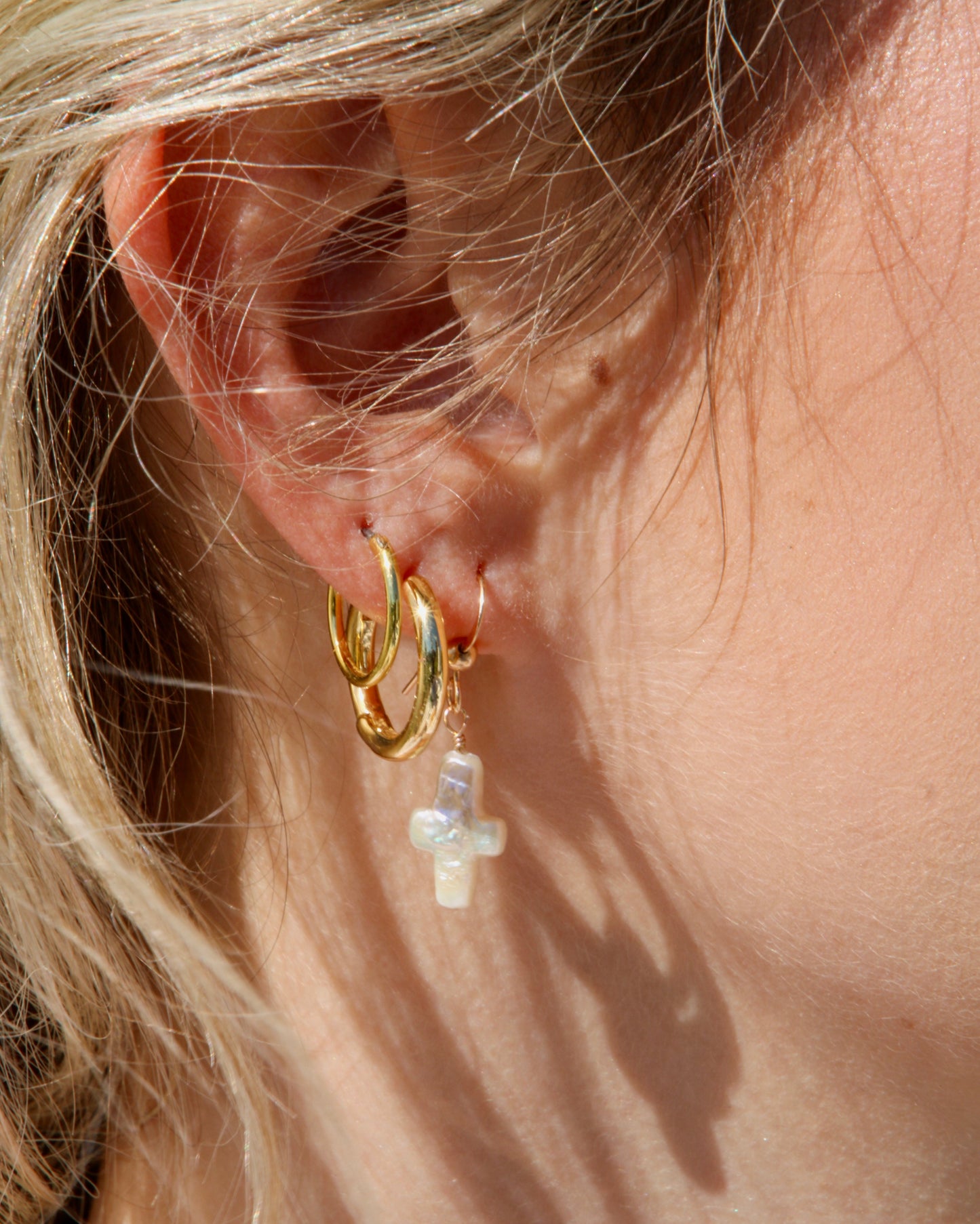 Close-up of a gold hoop earring with a cross charm worn by a person.
