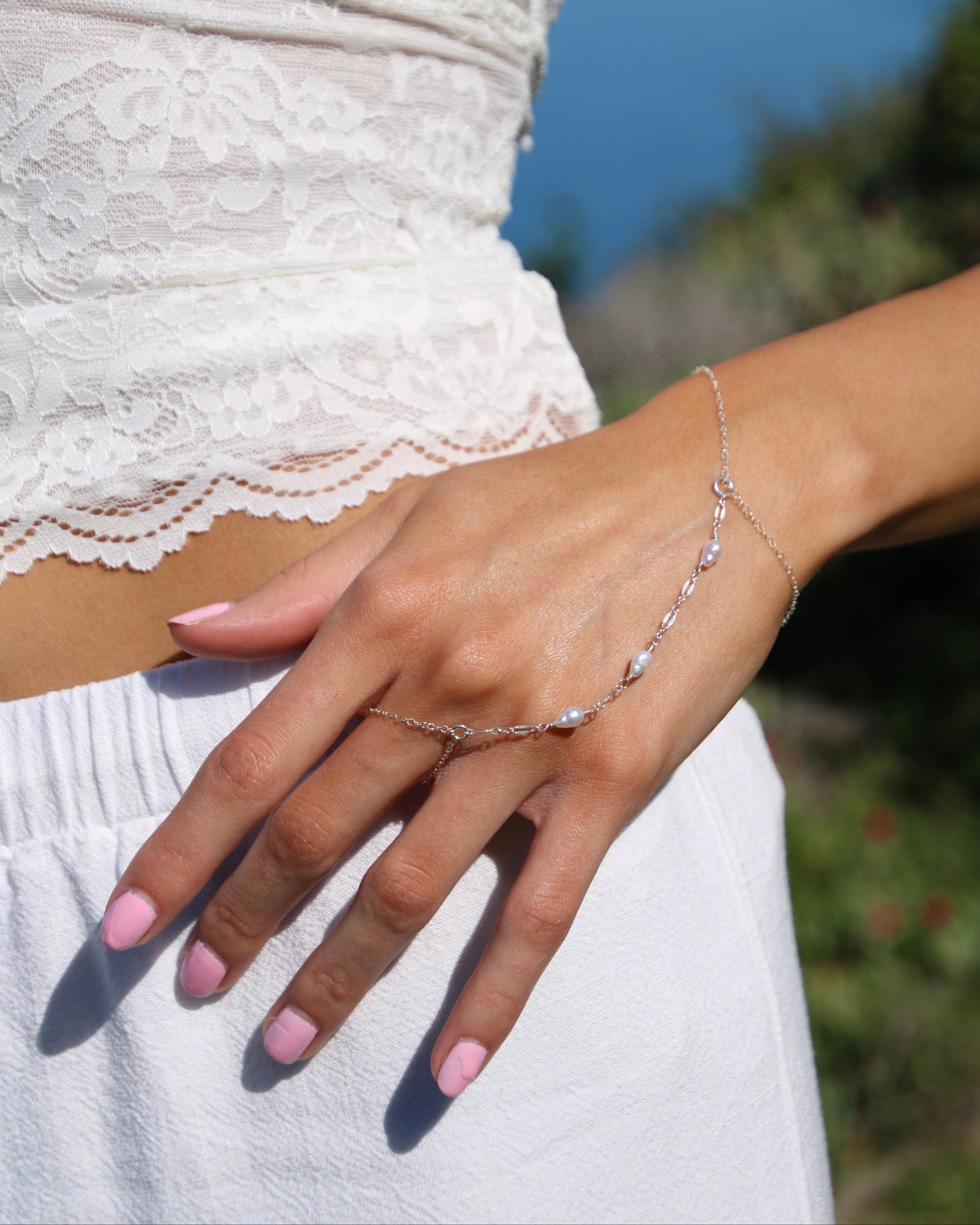 Close-up of a hand wearing a delicate bracelet with a blurred natural background