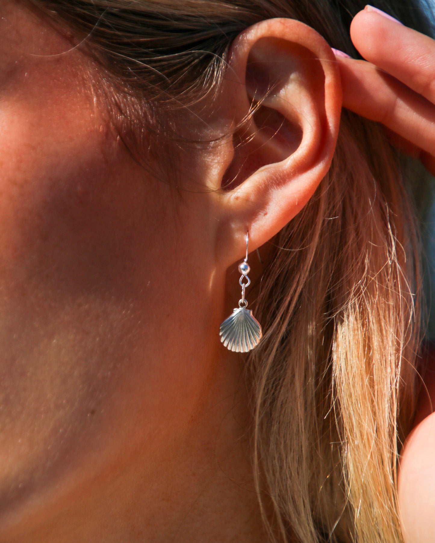 Close-up of an ear wearing a silver shell-shaped earring.